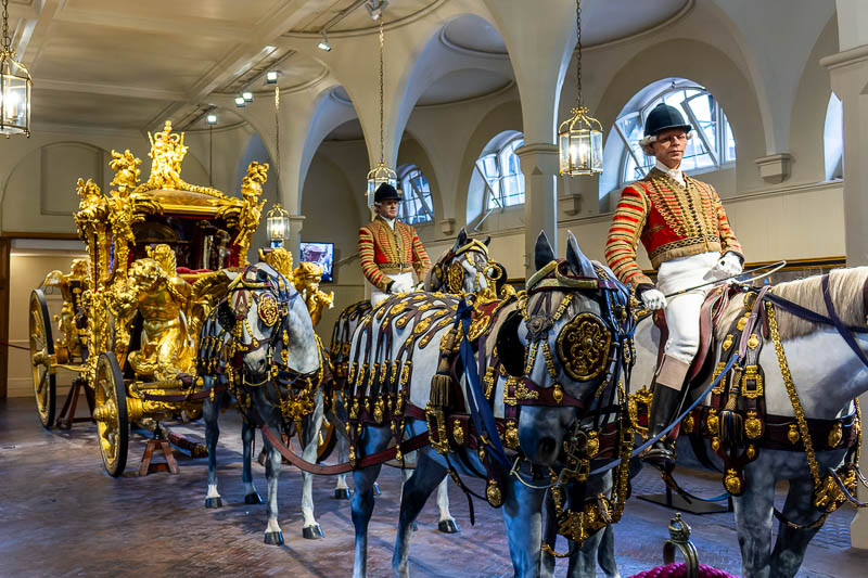 Lebensgroße Modelle der Windsor Grey Pferde und Postillione in roten Prunkuniformen vor der Gold State Coach in den Royal Mews. Zu sehen ist das detaillierte goldene Pferdegeschirr.