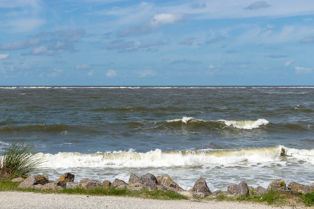 Wellen der Nordsee brechen am Strand vor einer Steinbefestigung.