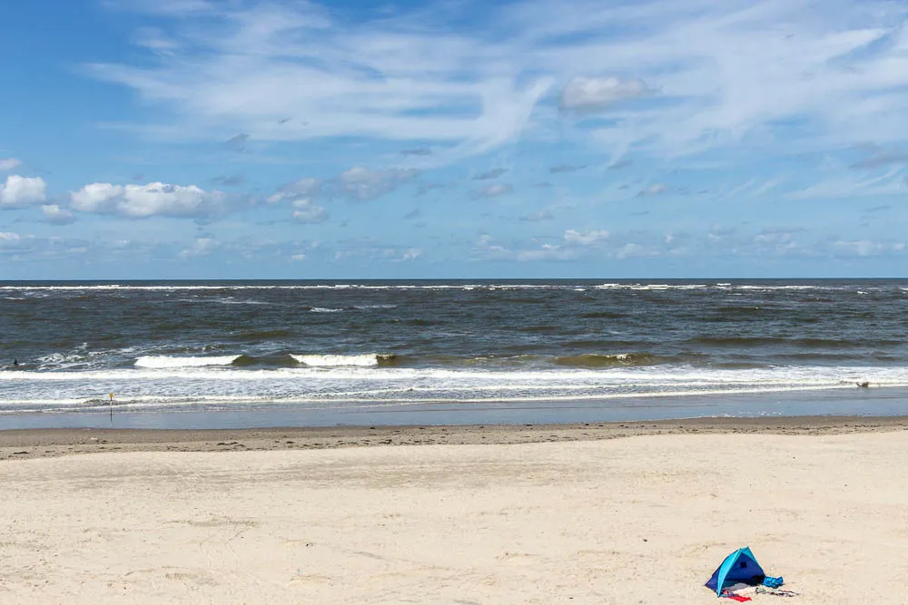 Weiter Sandstrand mit einzelnen Menschen und weitem Horizont.