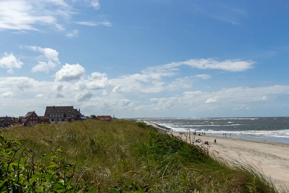 Blick vom Strand entlang der Küste mit Häusern und Dünen.